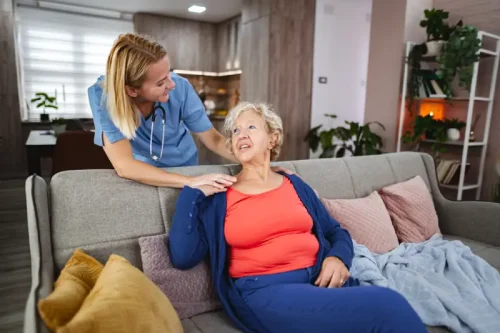 Female nurse caring for elderly woman on couch at home