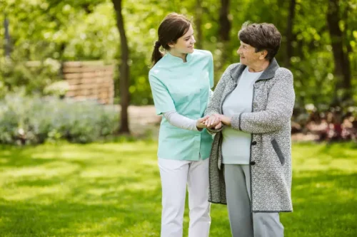 Caregiver assisting elderly woman walking in sunny park