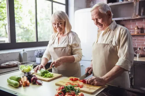 Senior couple smiling while chopping vegetables together in kitchen