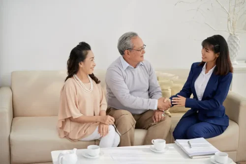 Professional woman shaking hands with senior couple on sofa