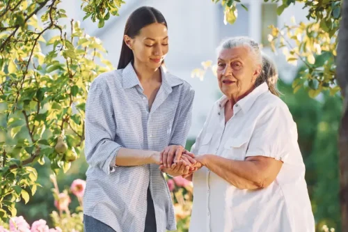 Young woman gently holding hands with elderly woman outdoors